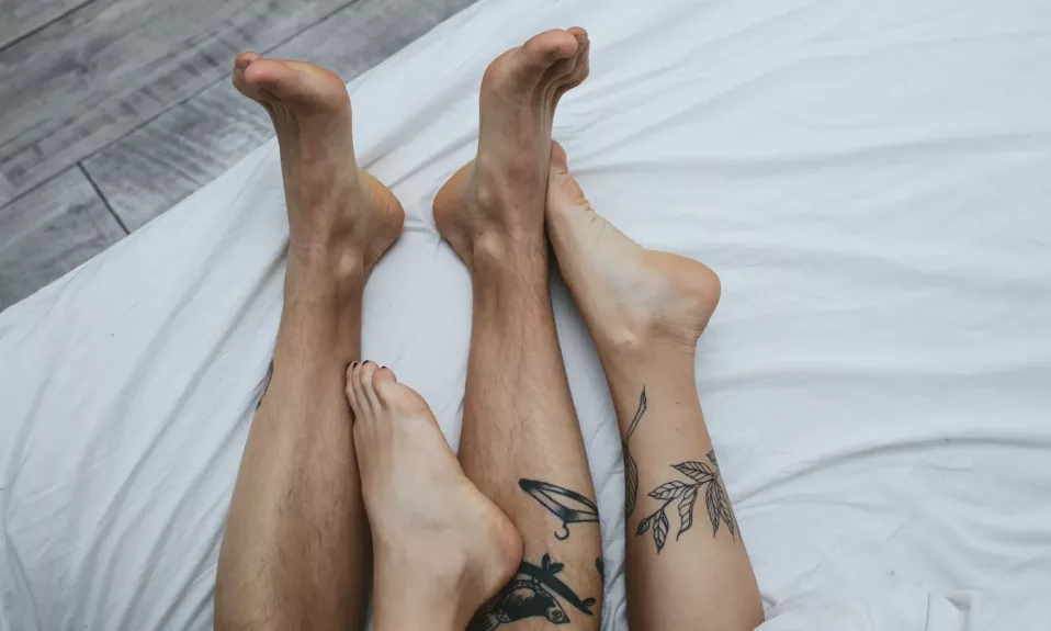 Pieds croisés avec tatouages sur lit blanc.